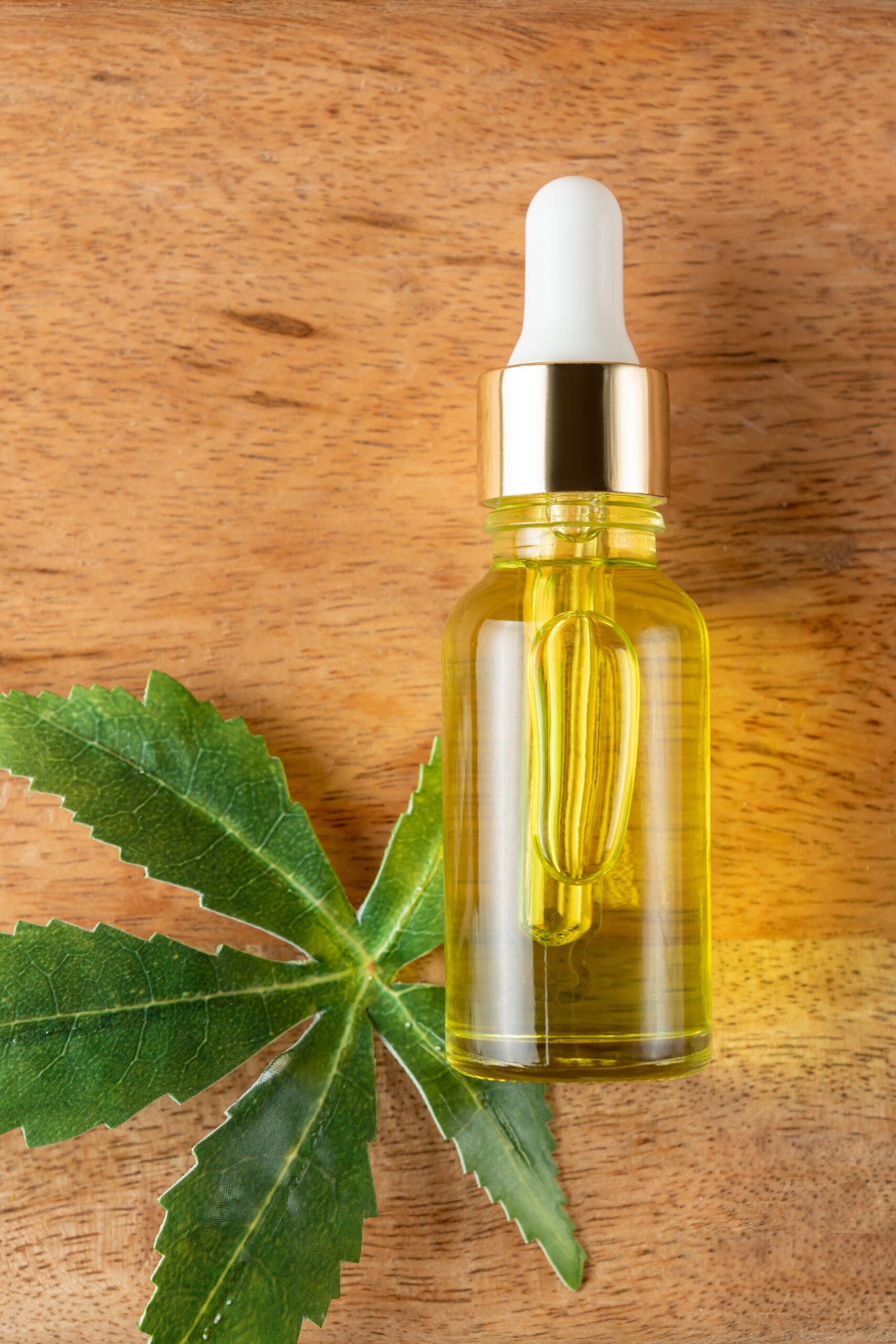 Cannabis leaf Serum, cosmetics, hemp oil. Bottle or vial with a dropper and hemp leaf on wooden board. Natural cosmetics concept.