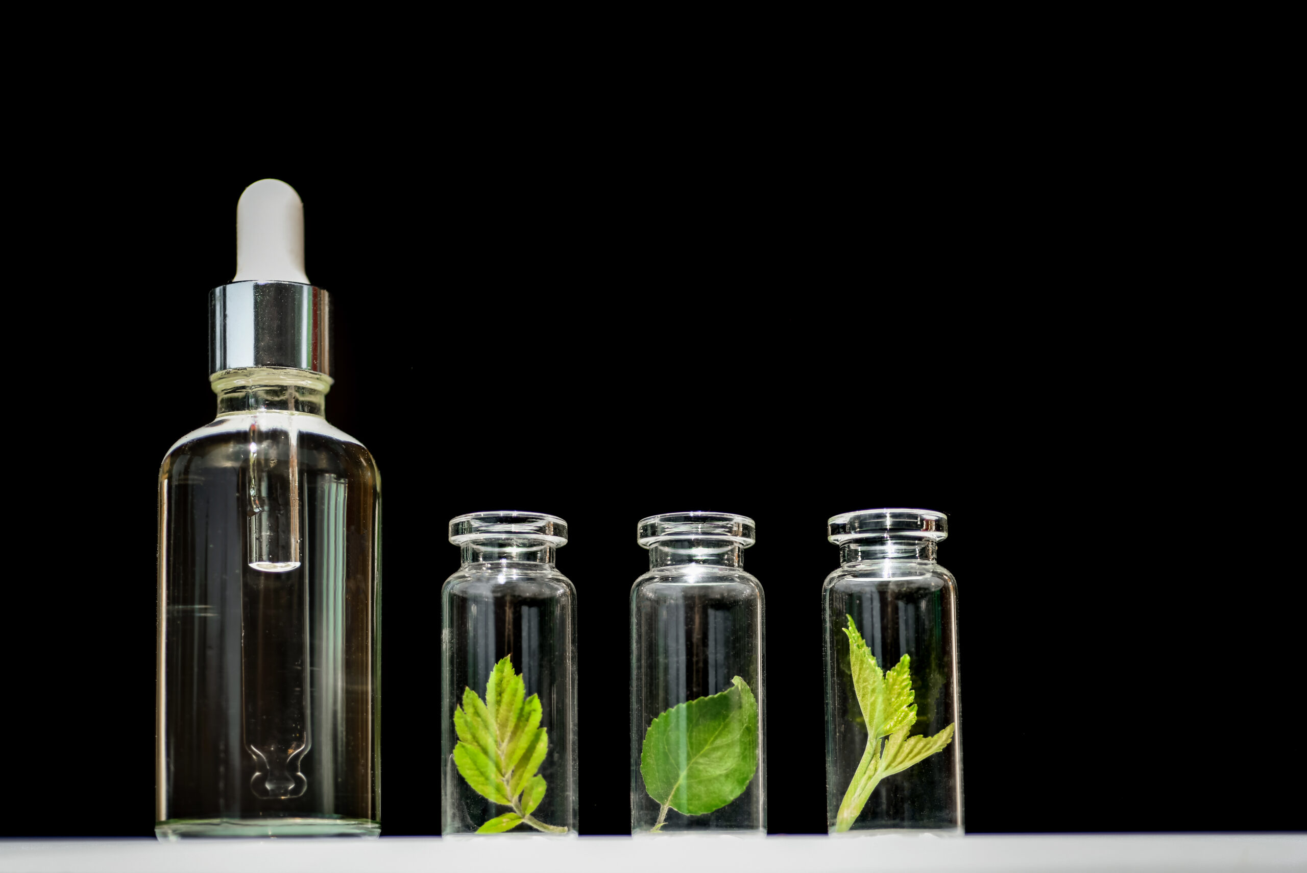 Homeopathic oil, serum and bottles with plants on blblack background