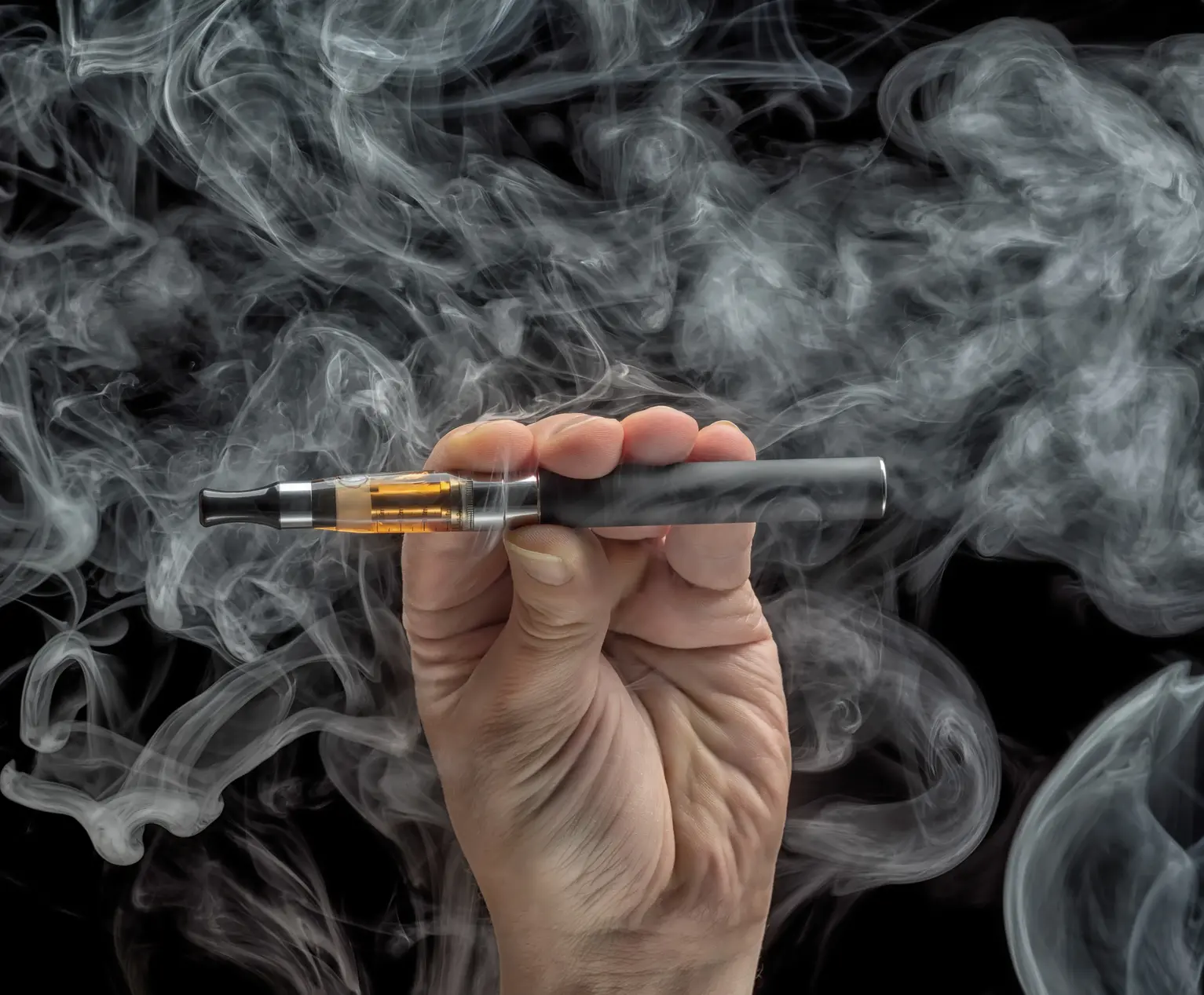 Person holding vape pen surrounded by vapor.